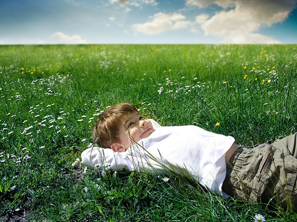 A boy lies in the grass and looks at the sky